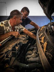 deux hommes sont penchés au dessus un moteur de voiture dans un atelier